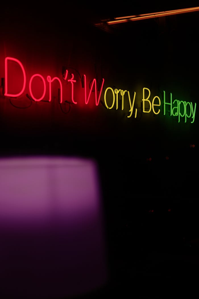 about-img Vibrant neon sign displaying 'Don't Worry, Be Happy' against a dark background.