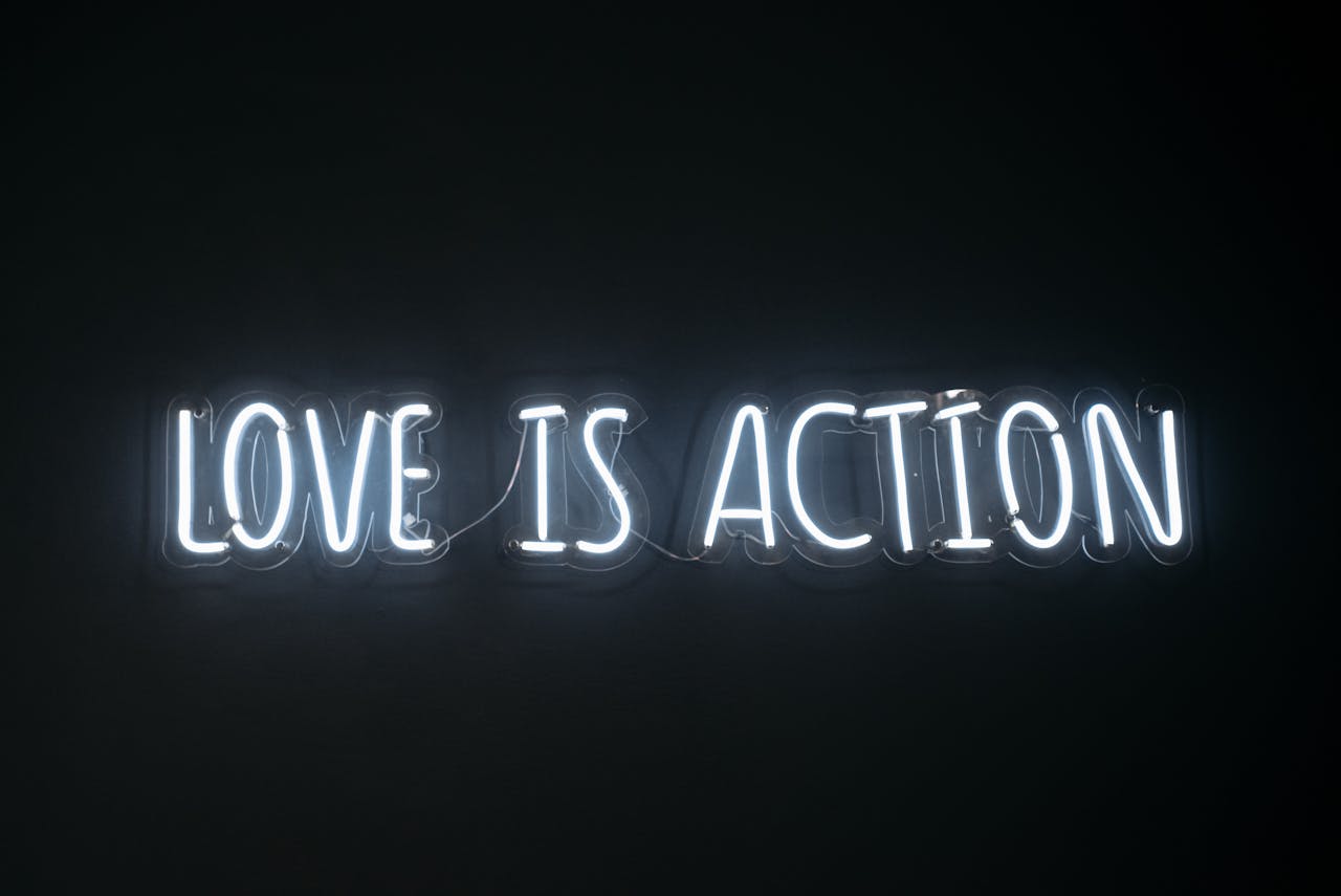 services-01 Bright neon sign reading 'Love is Action' against a dark background.